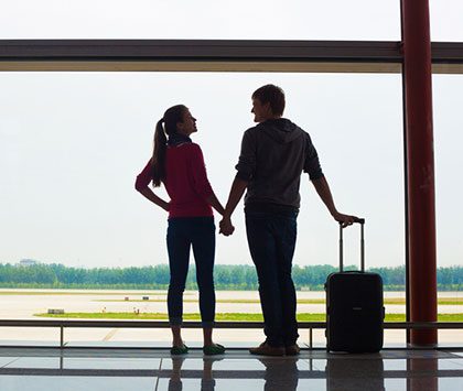 couple traveling by air stand together at airport ready for a flight with their luggage holding hands
